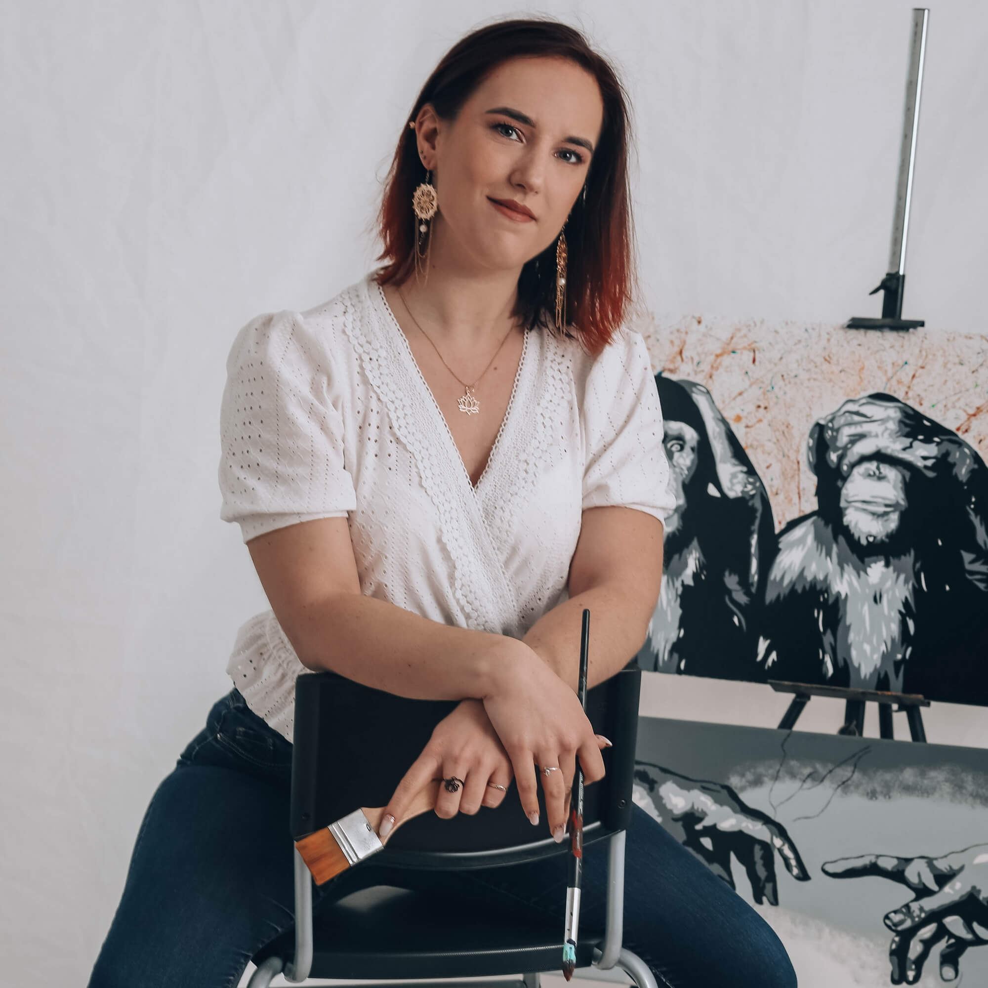 L'artiste au cœur de son univers, assise sur une chaise entourée de ses œuvres.